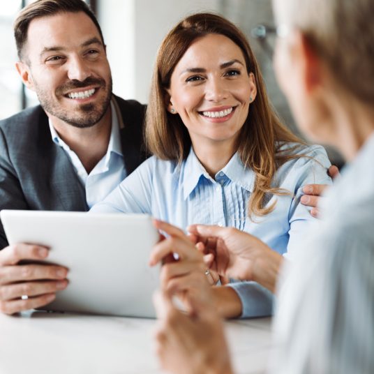 Young happy couple talking to their real estate agent on a business meeting in the office